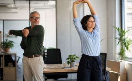 Zwei Kolleg:innen machen gemeinsam eine entspannte Bewegungspause im Büro, einer lockert Schultern und Nacken, der andere streckt sich, symbolisiert Bewegung im Büroalltag.